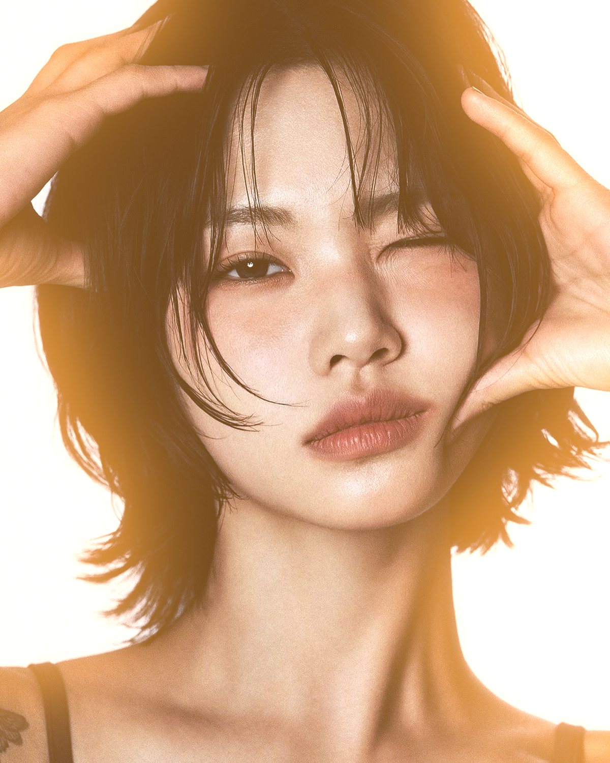 Soft glow effect on a portrait of a woman with black hair, hands on her head, made with the Glow Up filter in Filter Archive (Warm preset)