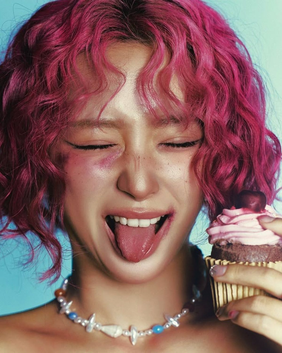 Soft glow effect on a portrait of a laughing woman with pink curly hair, made with the Glow Up filter in Filter Archive (Cool preset)